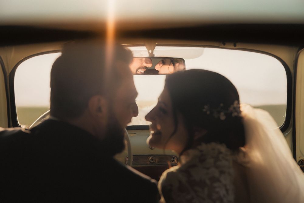 Antonio e Maddalena nell’auto d’epoca, illuminati dal sole attraverso il lunotto.
