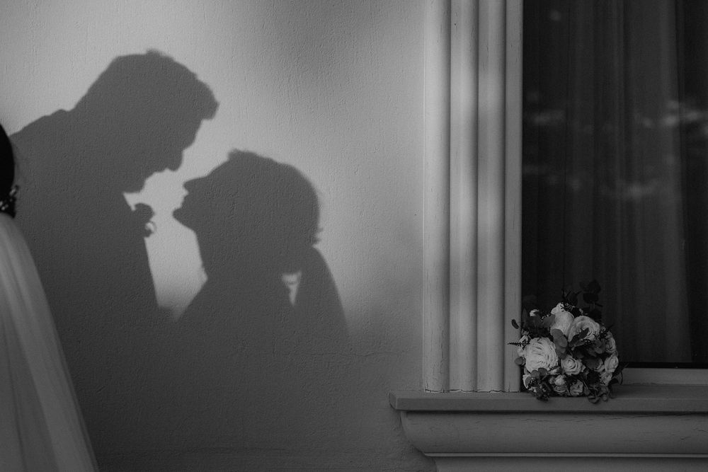 Le ombre degli sposi si incontrano sulla parete, accanto a una finestra e al bouquet.