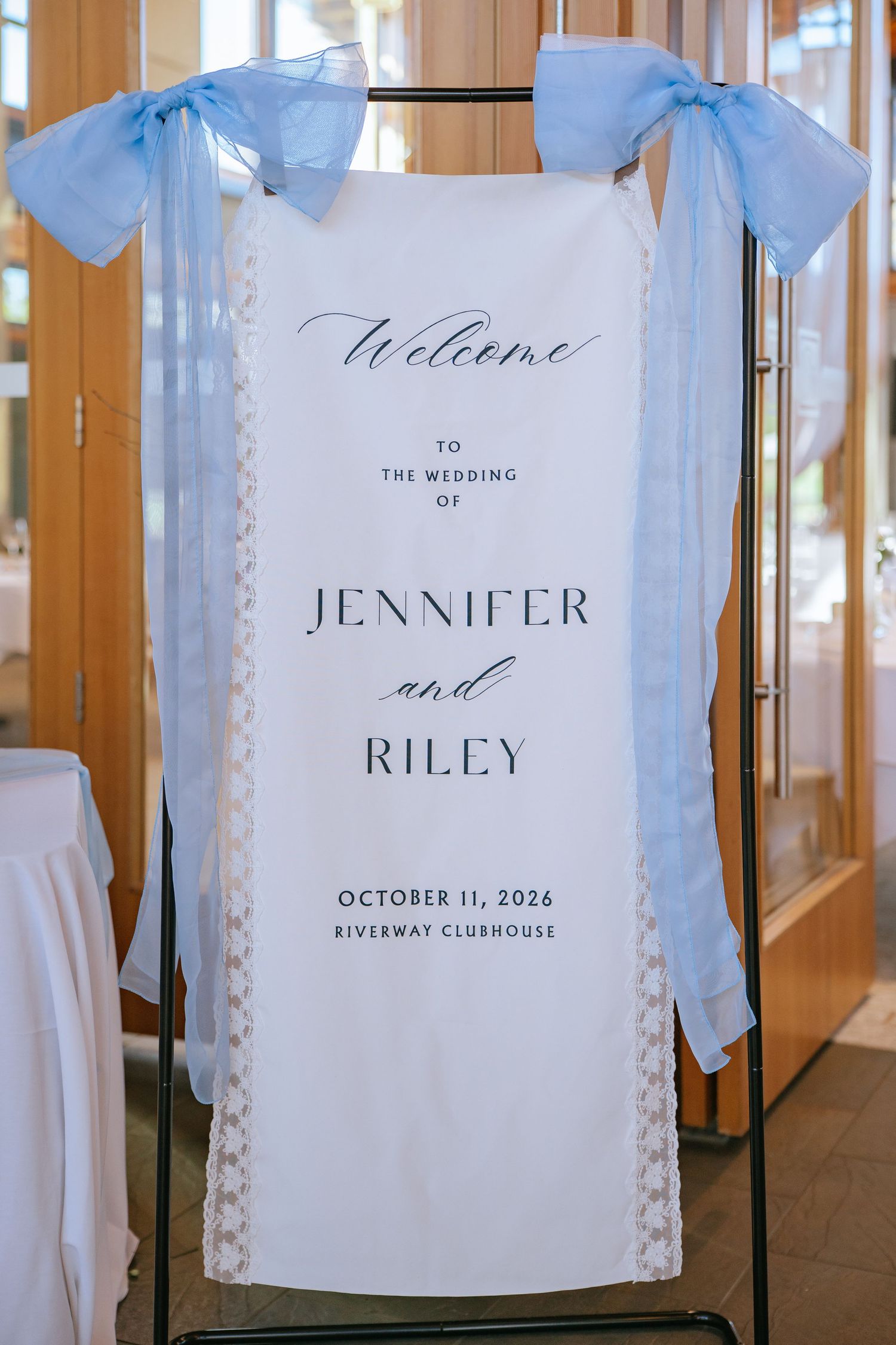 Wedding welcome sign reading Jennifer and Riley, October 11, 2026, Riverway Clubhouse with light blue bows