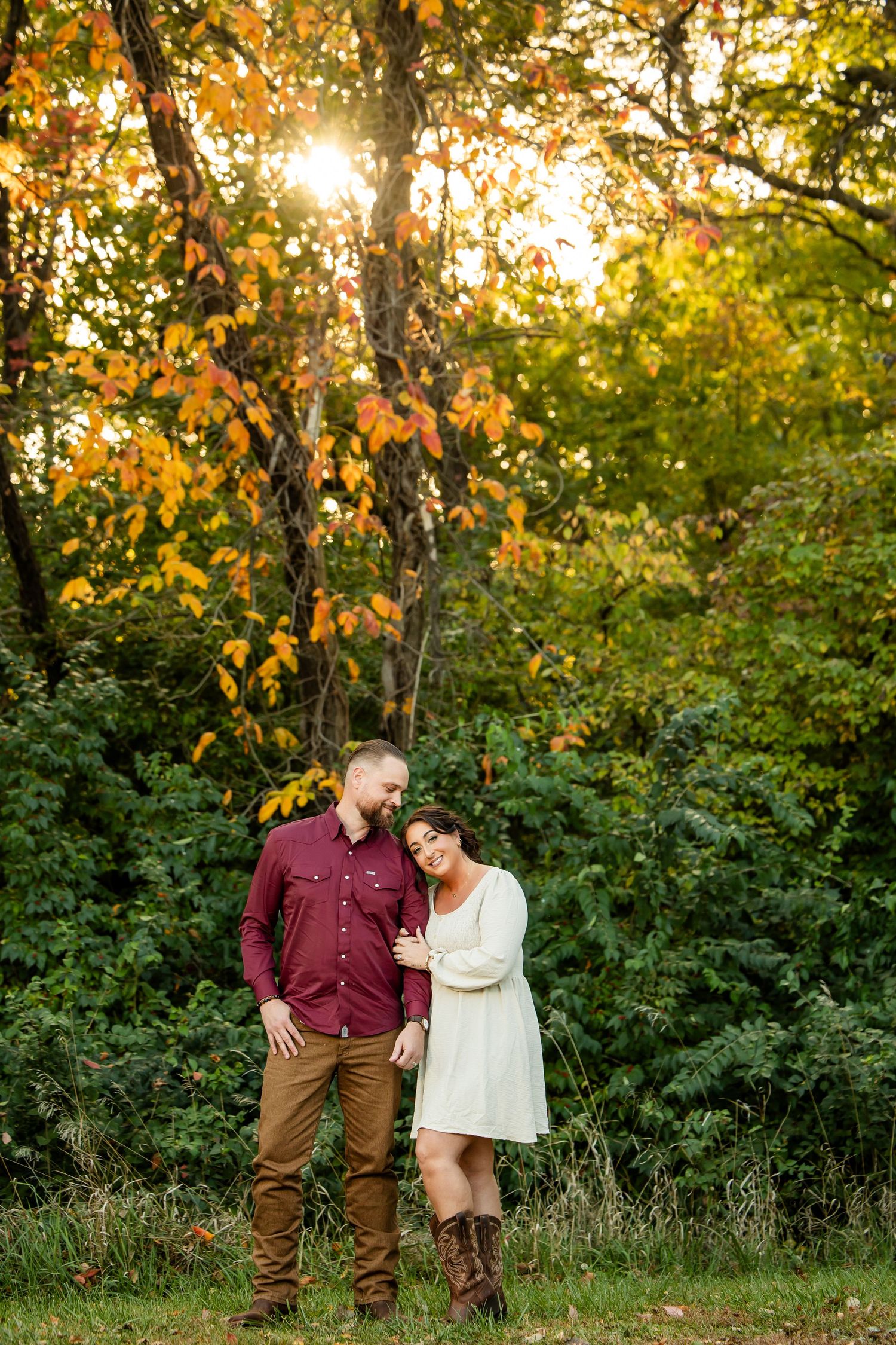 Couple embracing in autumn forest with golden sunlight filtering through colorful fall foliage.