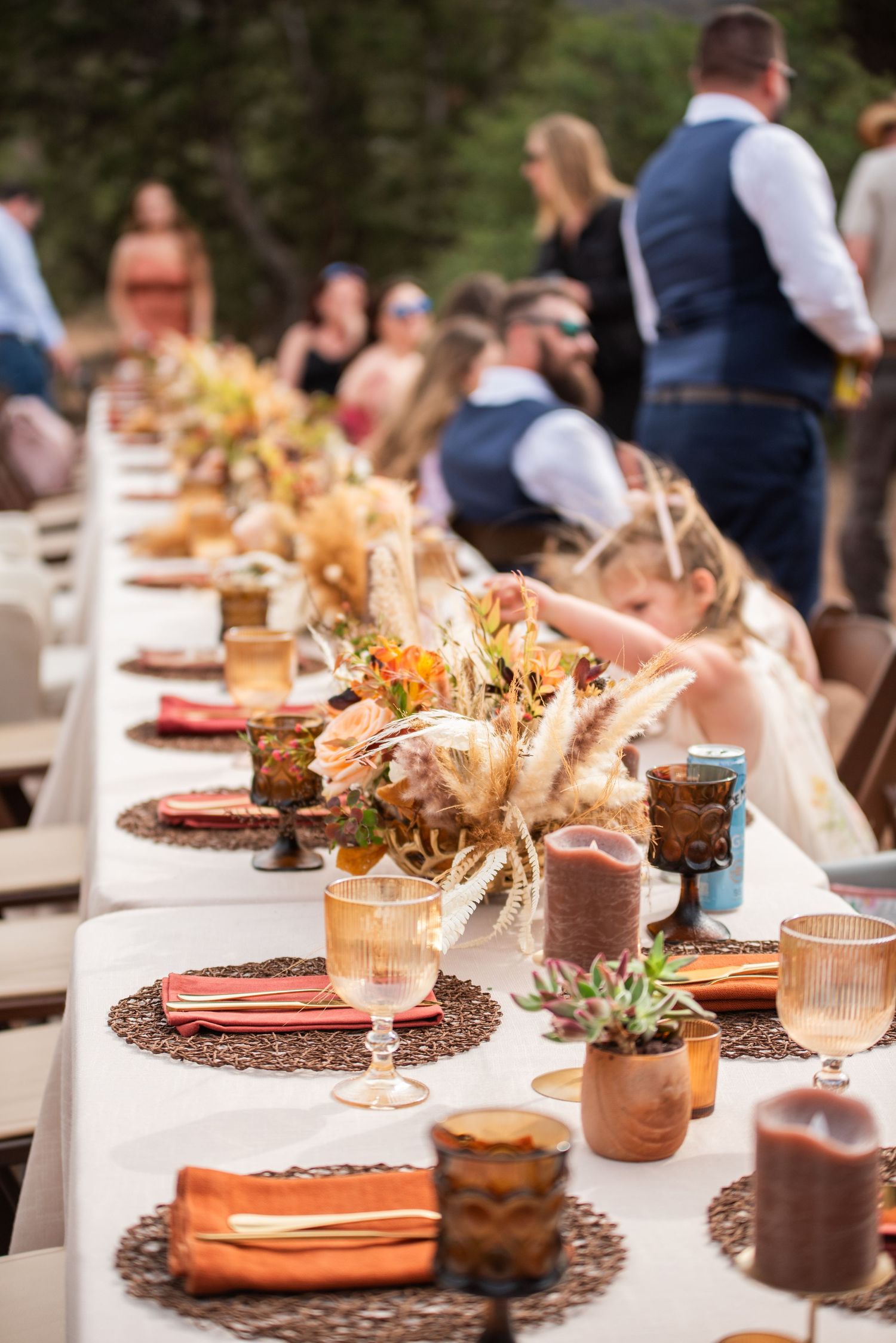 Elegant outdoor wedding reception table with rustic fall floral centerpieces, amber glassware, and woven charger plates.