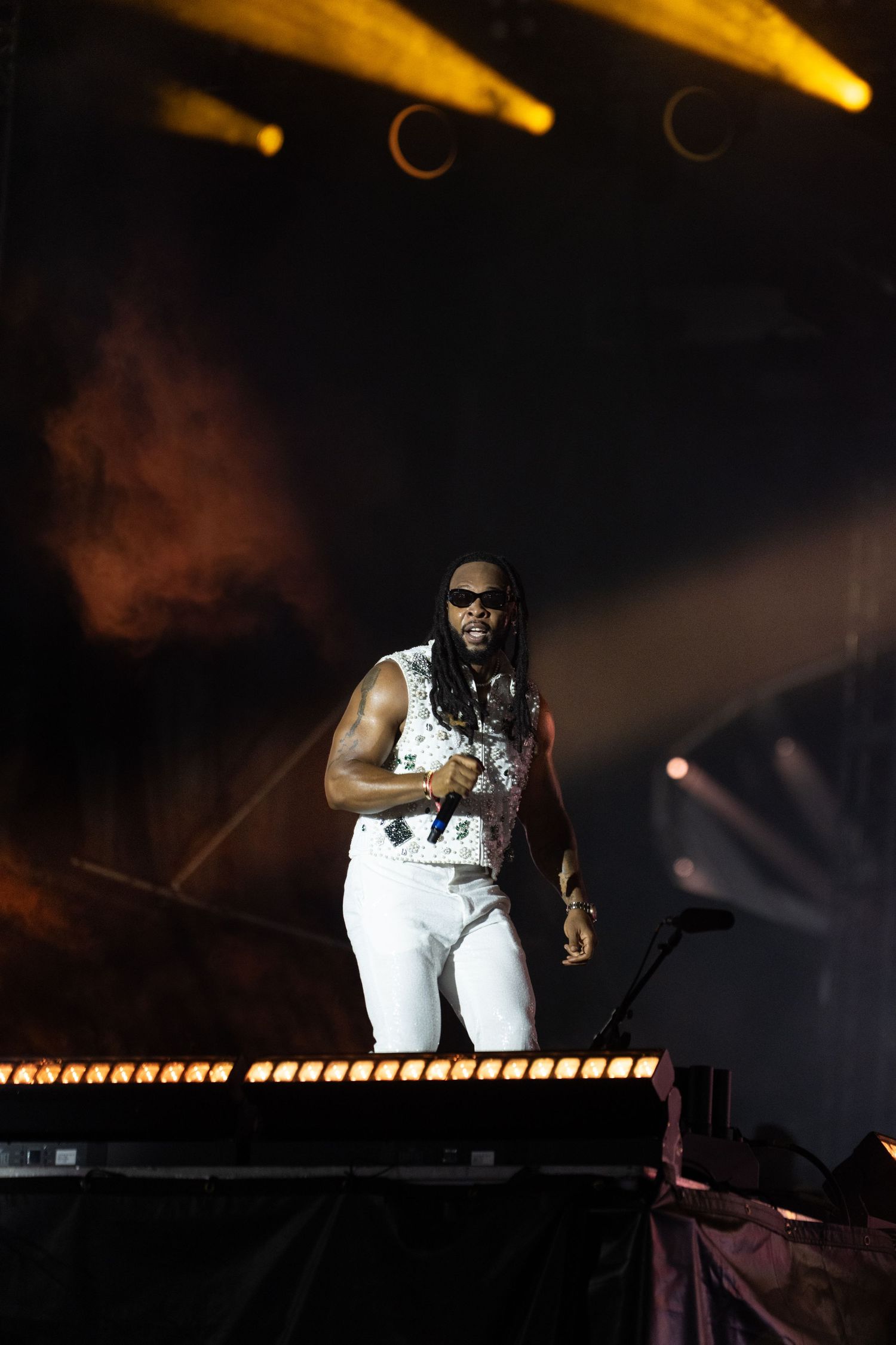 Male performer in white outfit singing on stage with dramatic yellow lighting and smoke effects at a live concert.