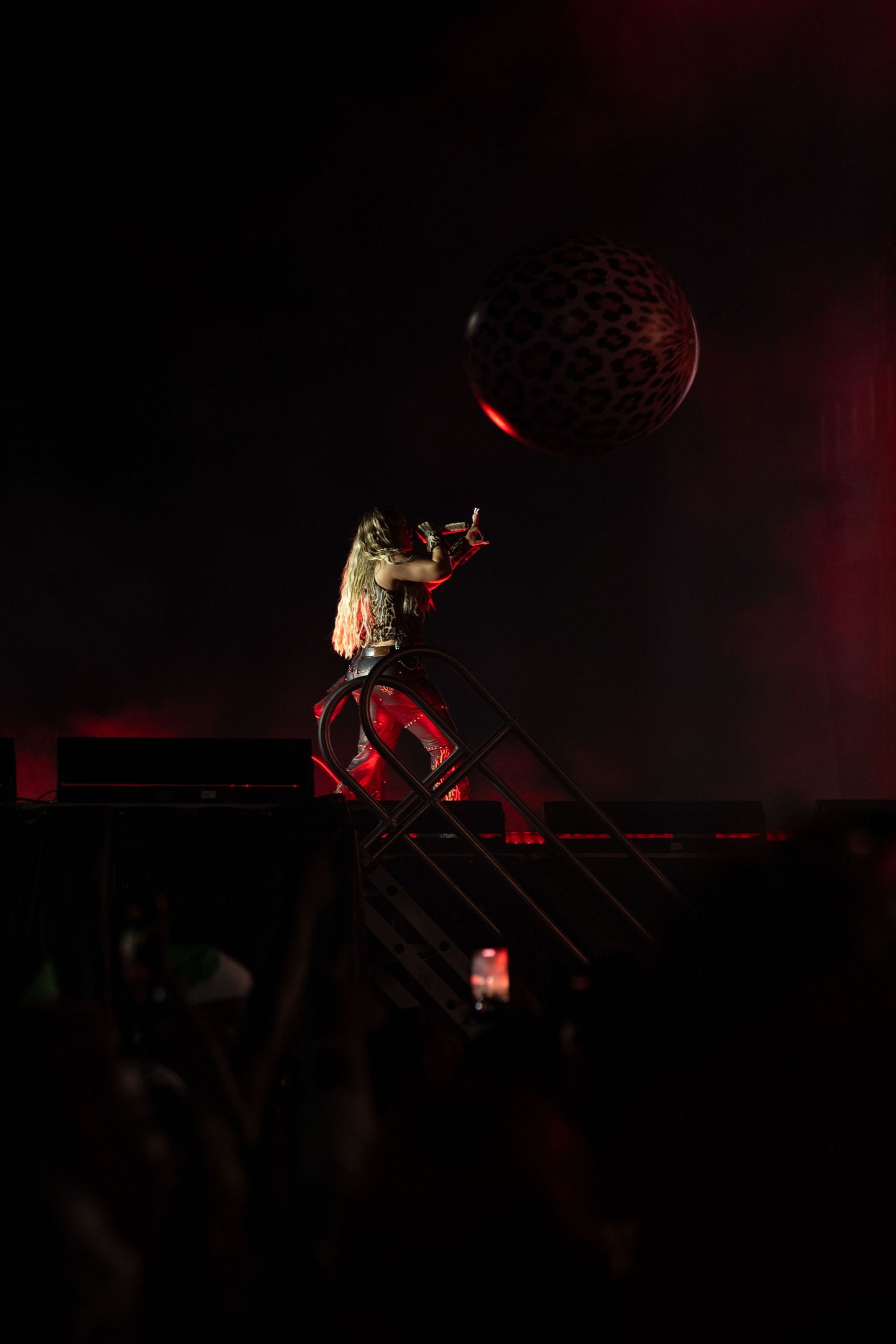 Performer on stage stairs with dramatic fire pyrotechnics blazing behind them during a live concert at night.