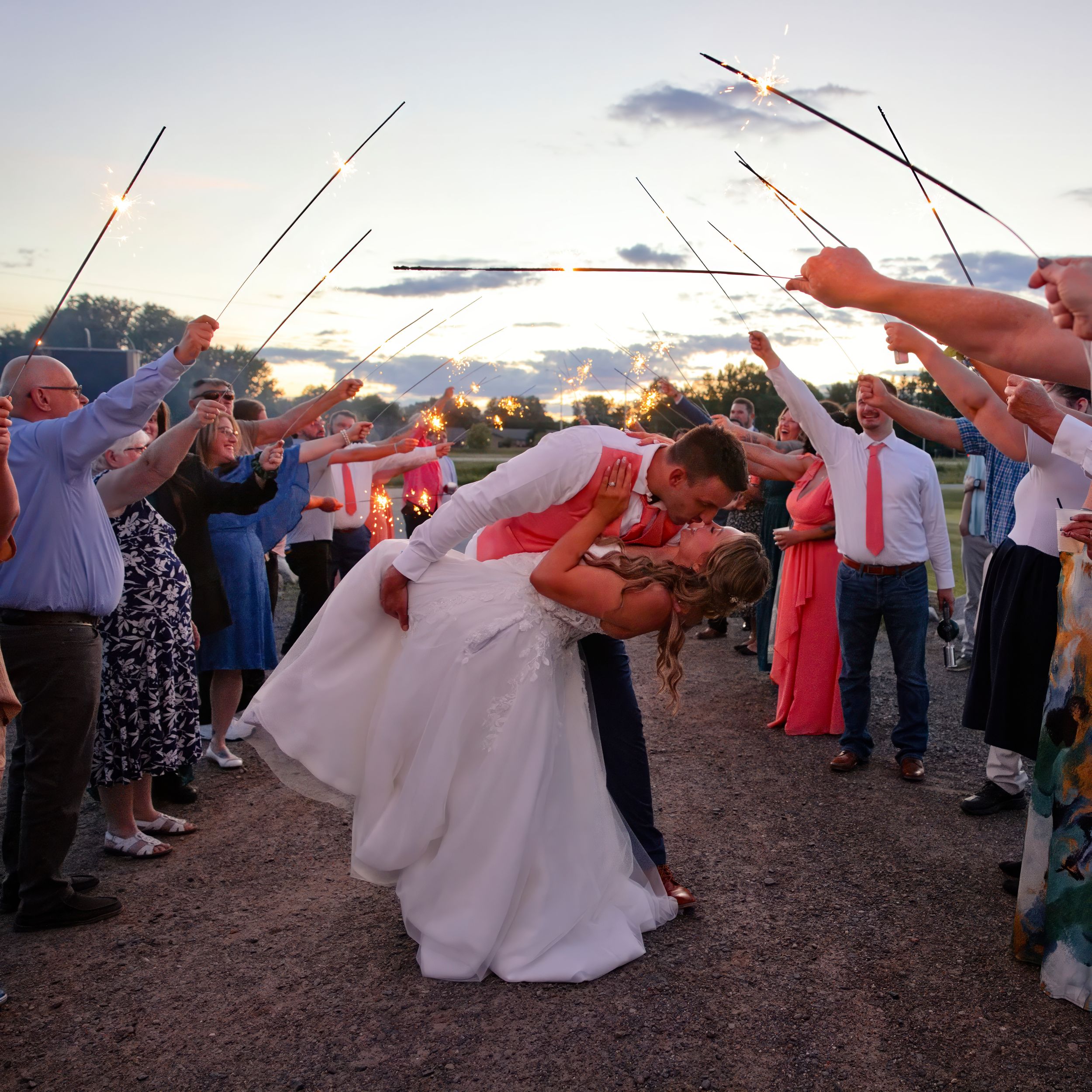 Bride and groom share a romantic dip kiss surrounded by guests holding sparklers at an outdoor wedding celebration.