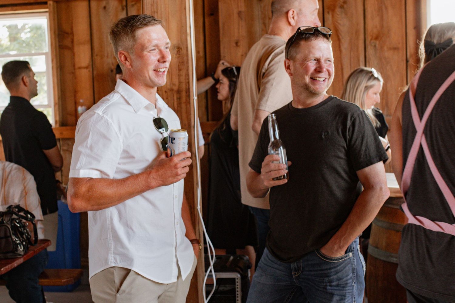 Two smiling men holding drinks chat at a casual indoor social gathering event.