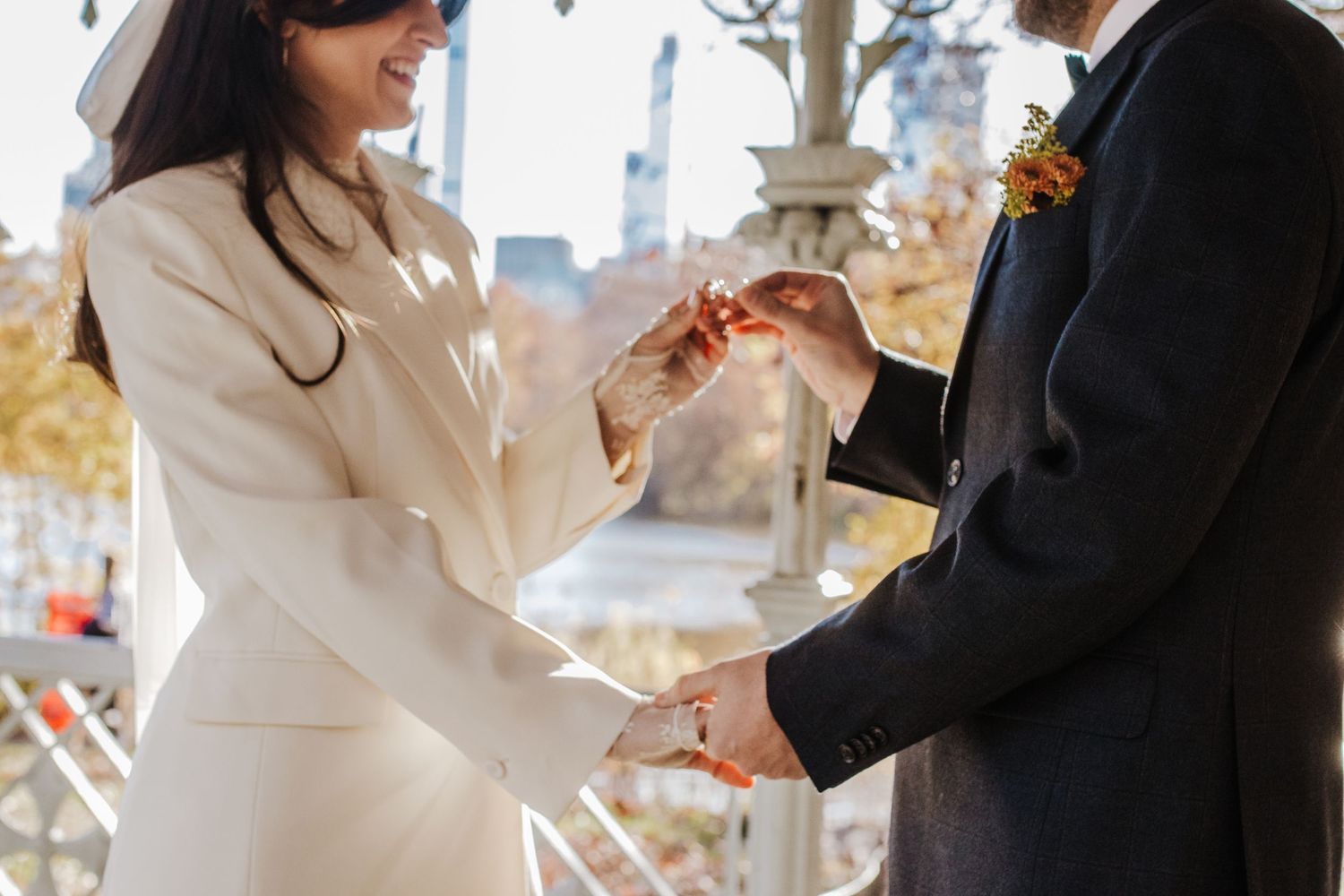 Bride in white coat exchanges rings with groom in black suit during outdoor wedding ceremony in autumn.