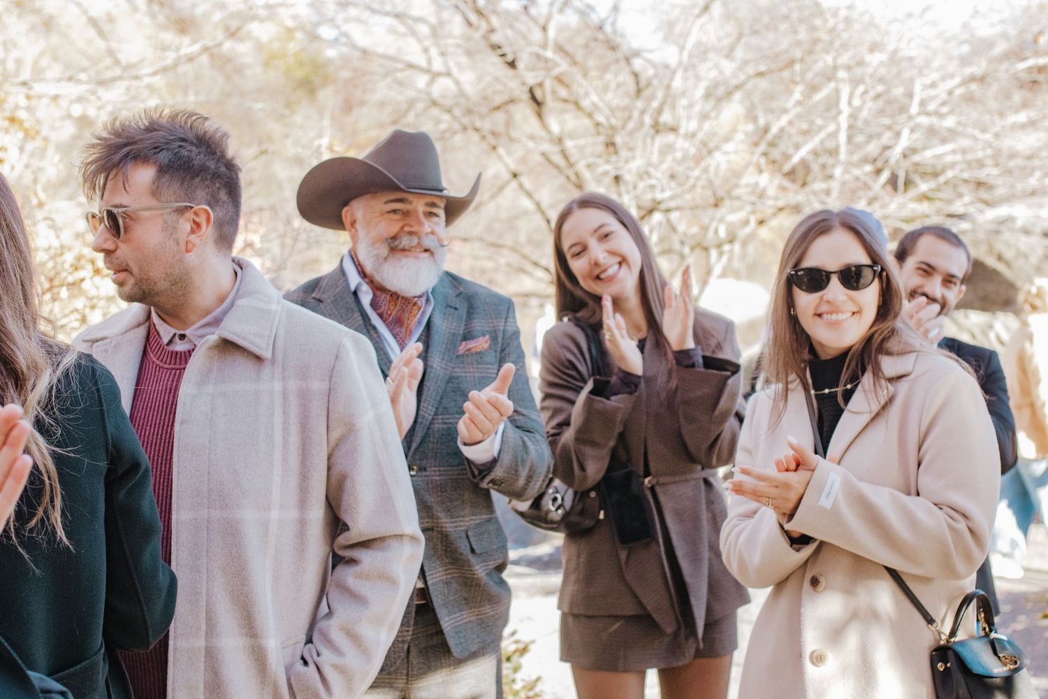 Group of stylish adults socializing outdoors in winter, man in cowboy hat gesturing while others smile.
