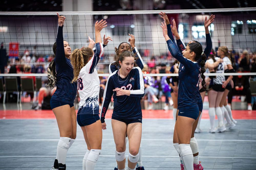 Female volleyball players celebrate together on indoor court, raising hands in victory during a competitive match.
