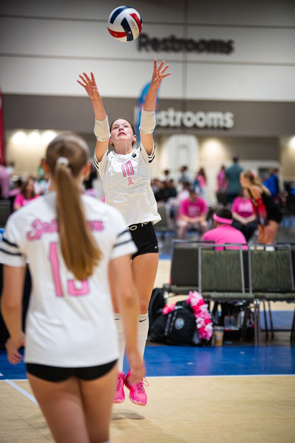 Young female volleyball player in white jersey sets the ball during an indoor tournament game.