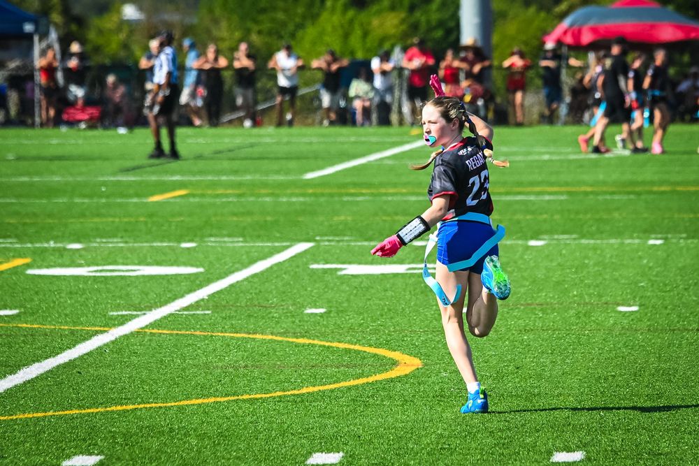 Female athlete wearing number 23 jersey sprinting on a green turf field during an outdoor ultimate frisbee tournament.