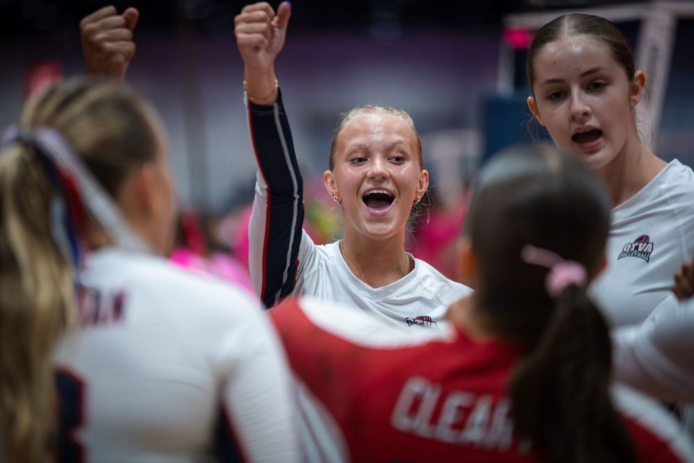 Volleyball players celebrate together on court, with one athlete raising her fist in excitement during a competitive match.