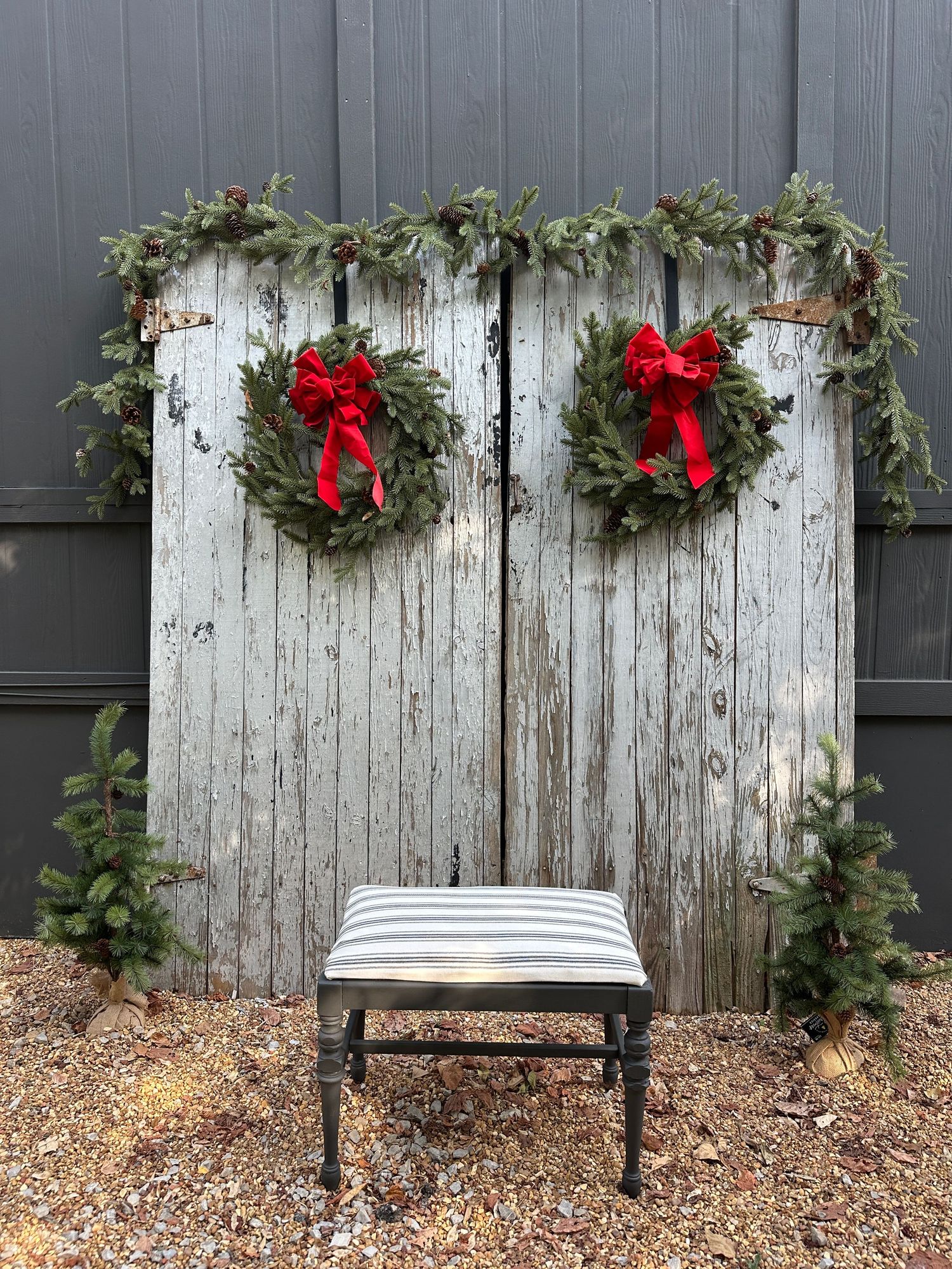 Rustic whitewashed barn doors decorated with Christmas wreaths, red bows, garland, and a striped bench for holiday photos.