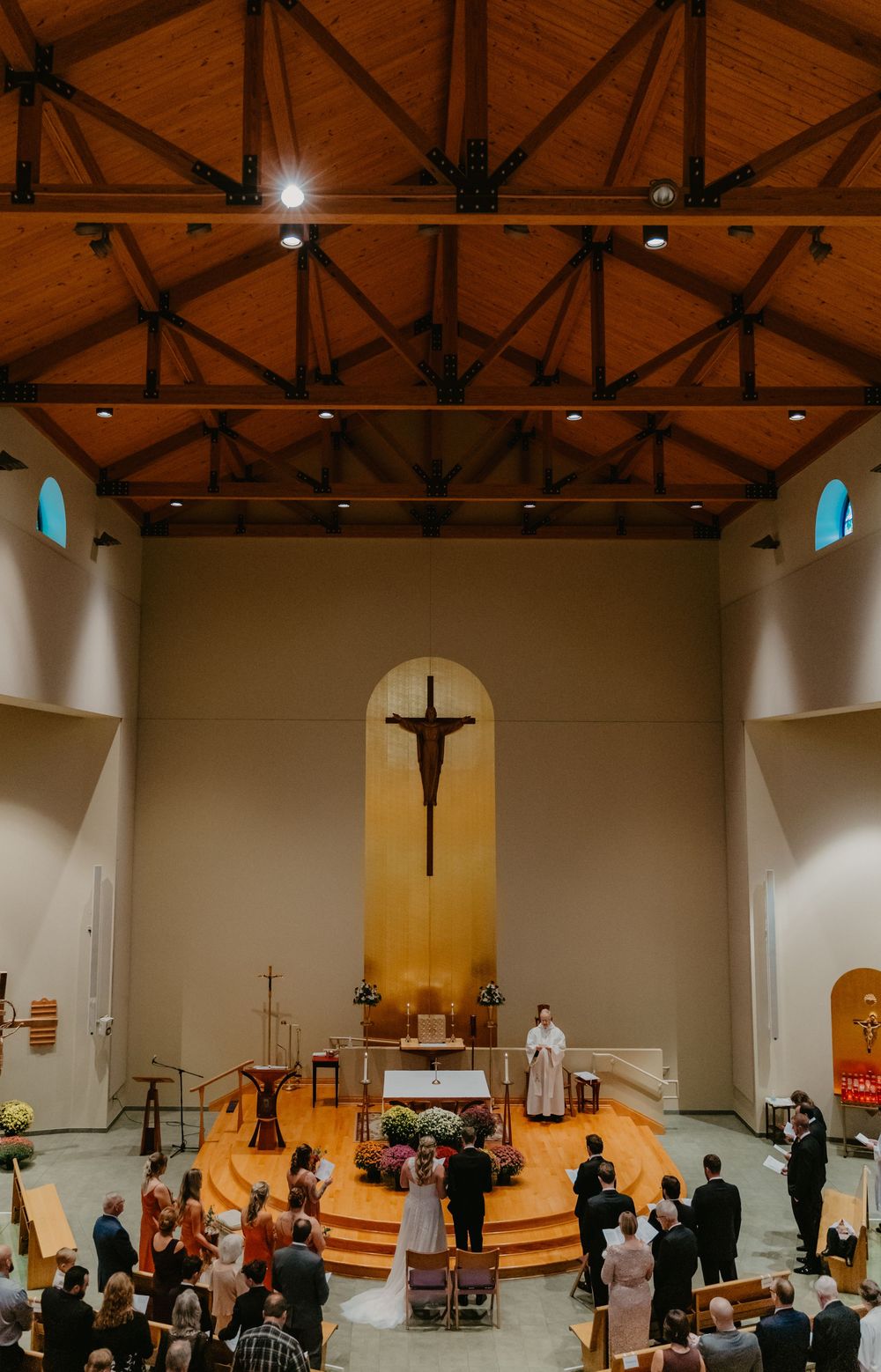 Aerial view of a wedding ceremony inside a modern church with wooden ceiling and crucifix above the altar.