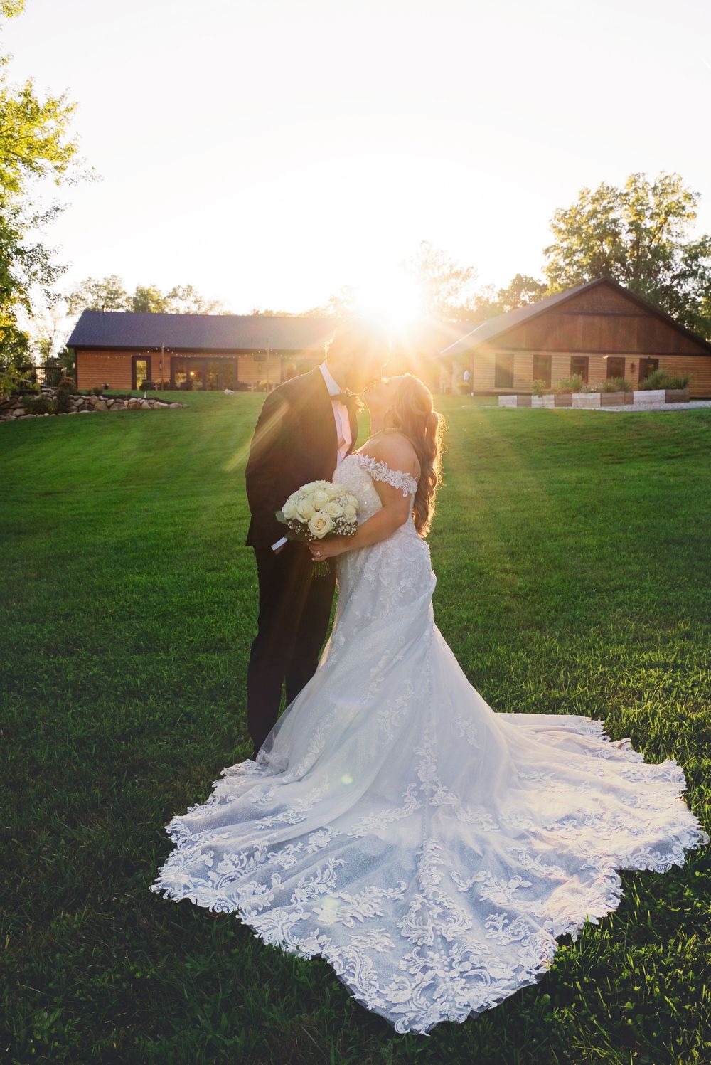 Sunset wedding portrait by a Southwest Michigan photo and video team at Augusta Creek venue as the sun flares behind them.