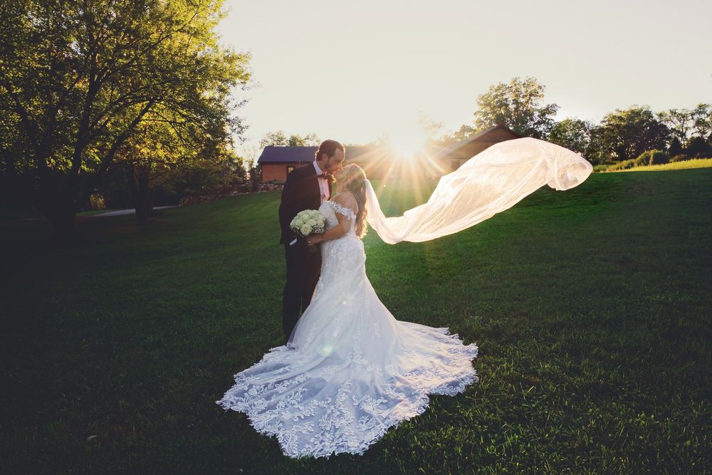 Bride & groom kissing at sunset on the lawn at Augusta Creek wedding venue in Delton, Michigan, with a long, floating veil.