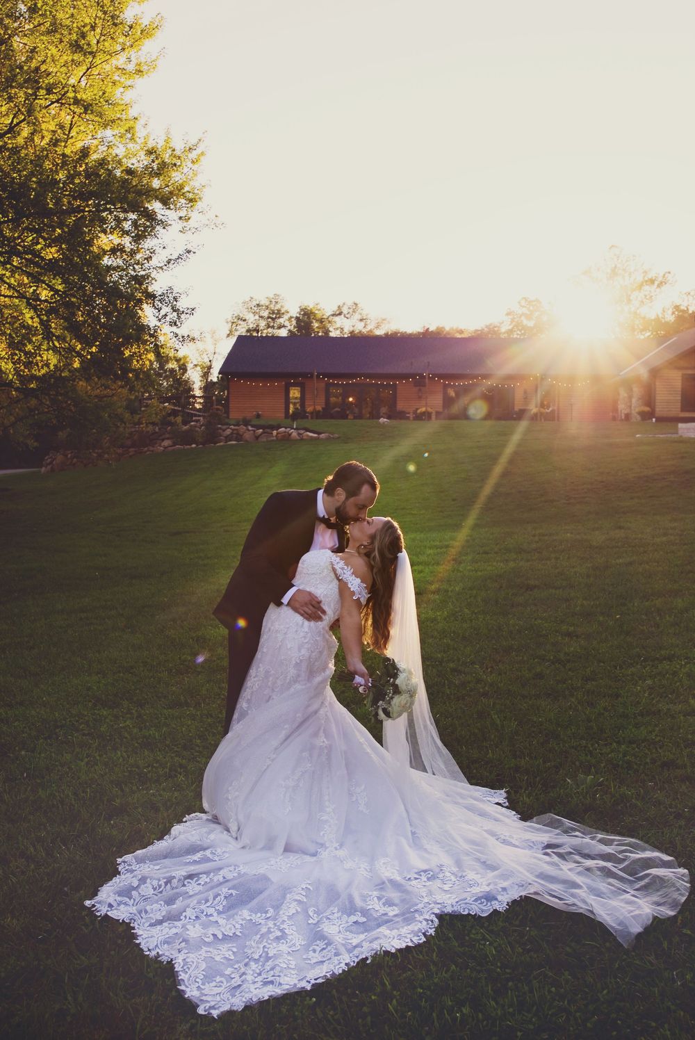Bride and groom dip-kiss at sunset at Augusta Creek wedding venue as the sun flares behind them.