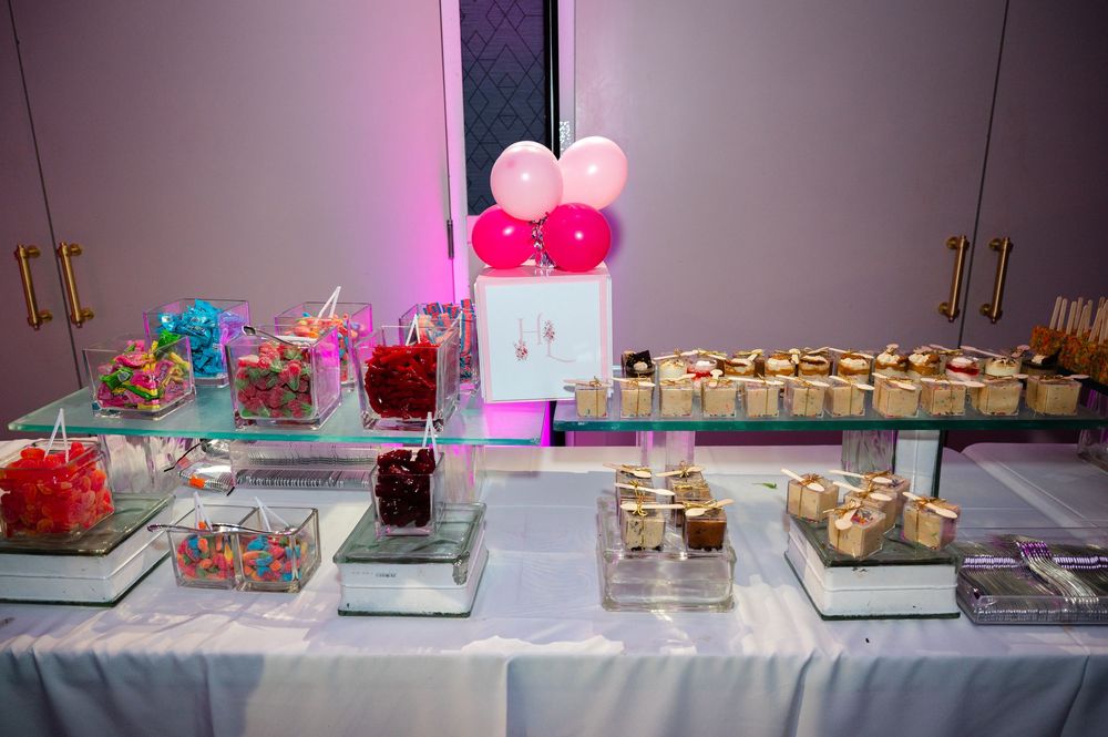 Glass candy buffet table with colorful sweets, dessert cups, and pink and white balloons at an elegant party reception.