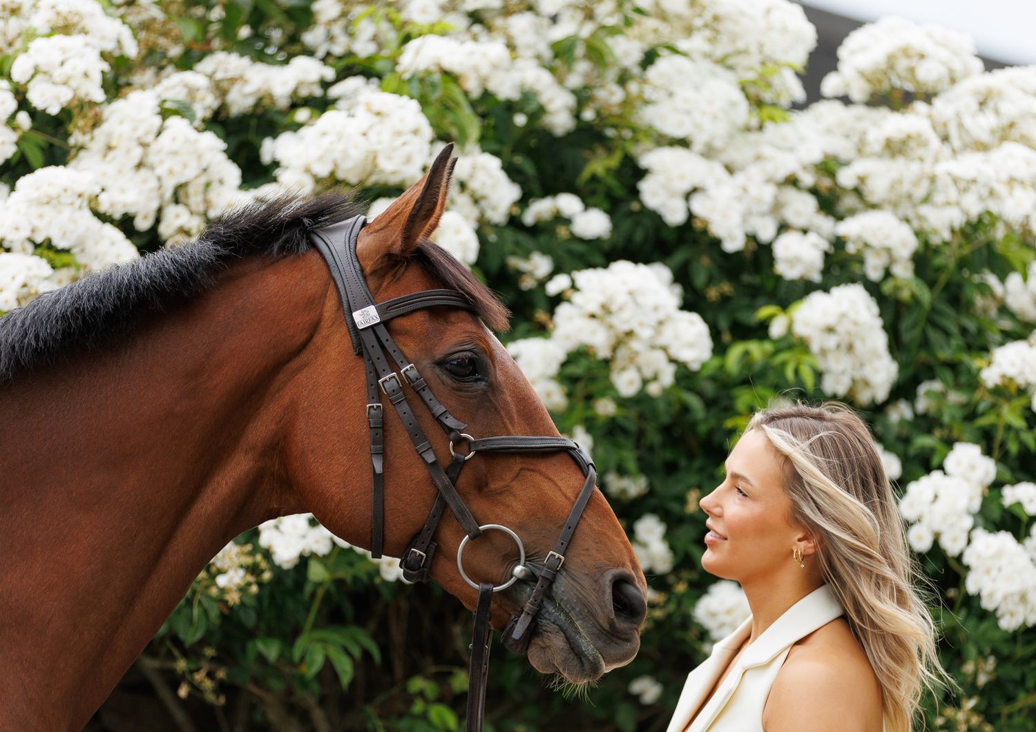 Woman leading a dark brown horse along a lush green garden path beside a tranquil pond.