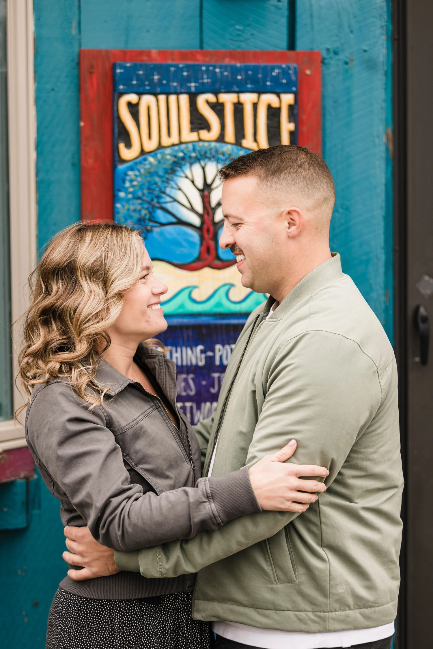 Couple embracing and gazing at each other in front of a colorful mural.  Engagement at Rockport Harbor, Rockport, MA