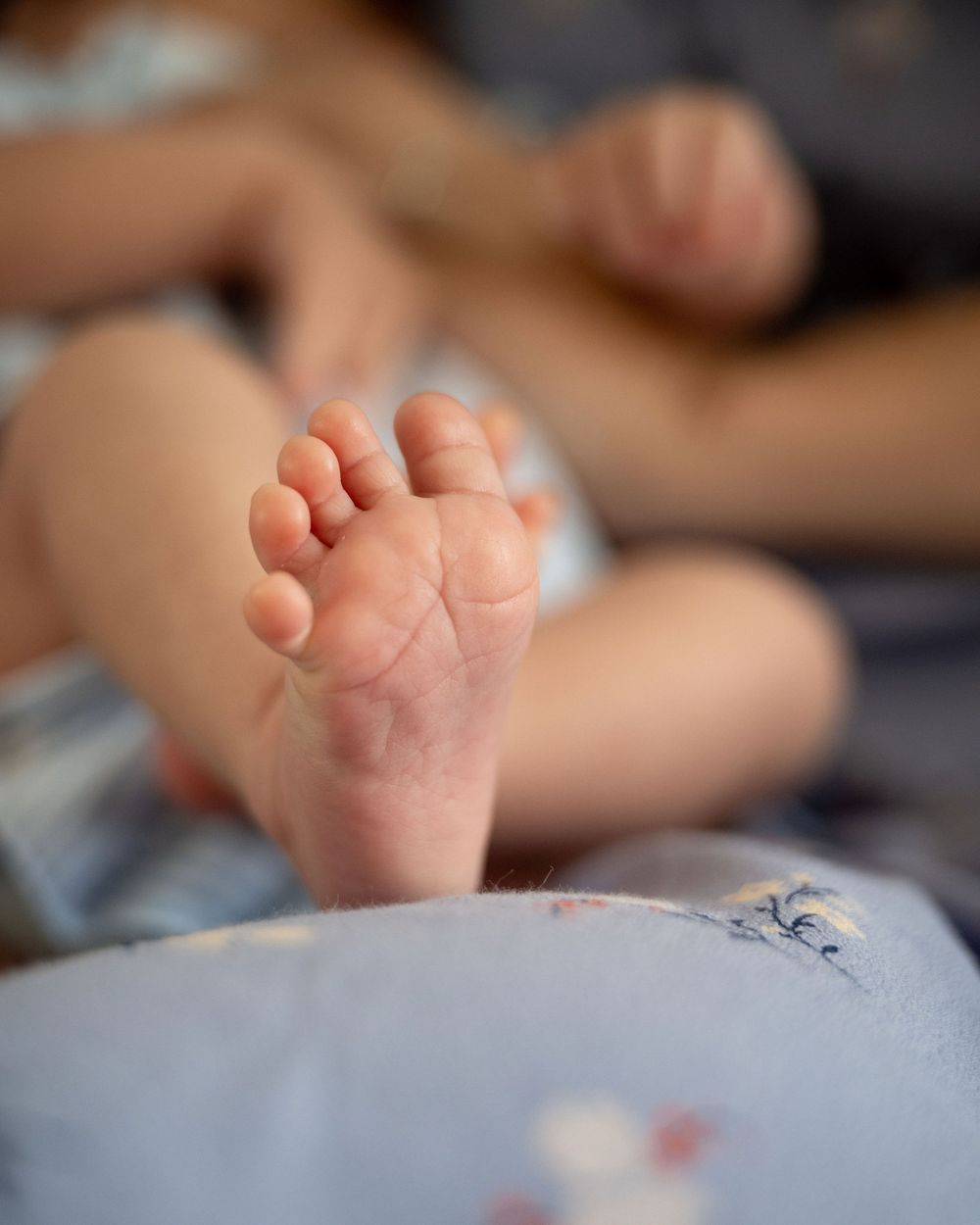 Close-up of a newborn baby's tiny bare foot resting on a soft blue blanket with a blurred person in the background.