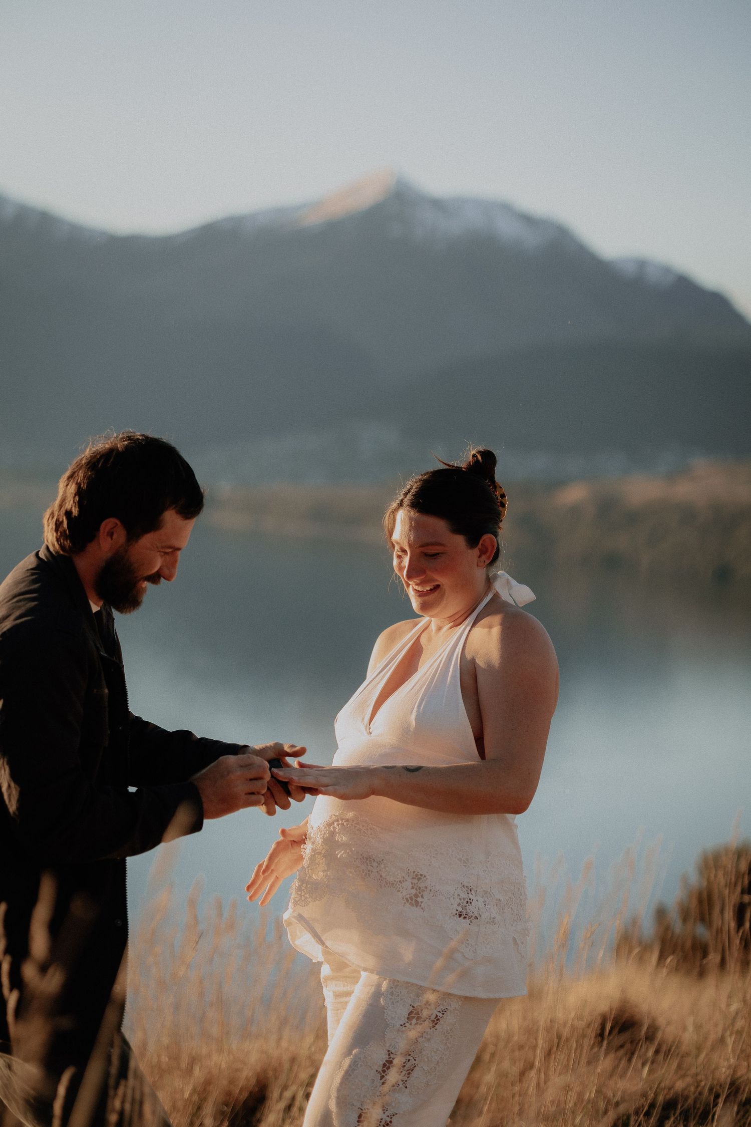Couple exchanging rings during outdoor elopement ceremony with misty mountain lake backdrop at golden hour.
