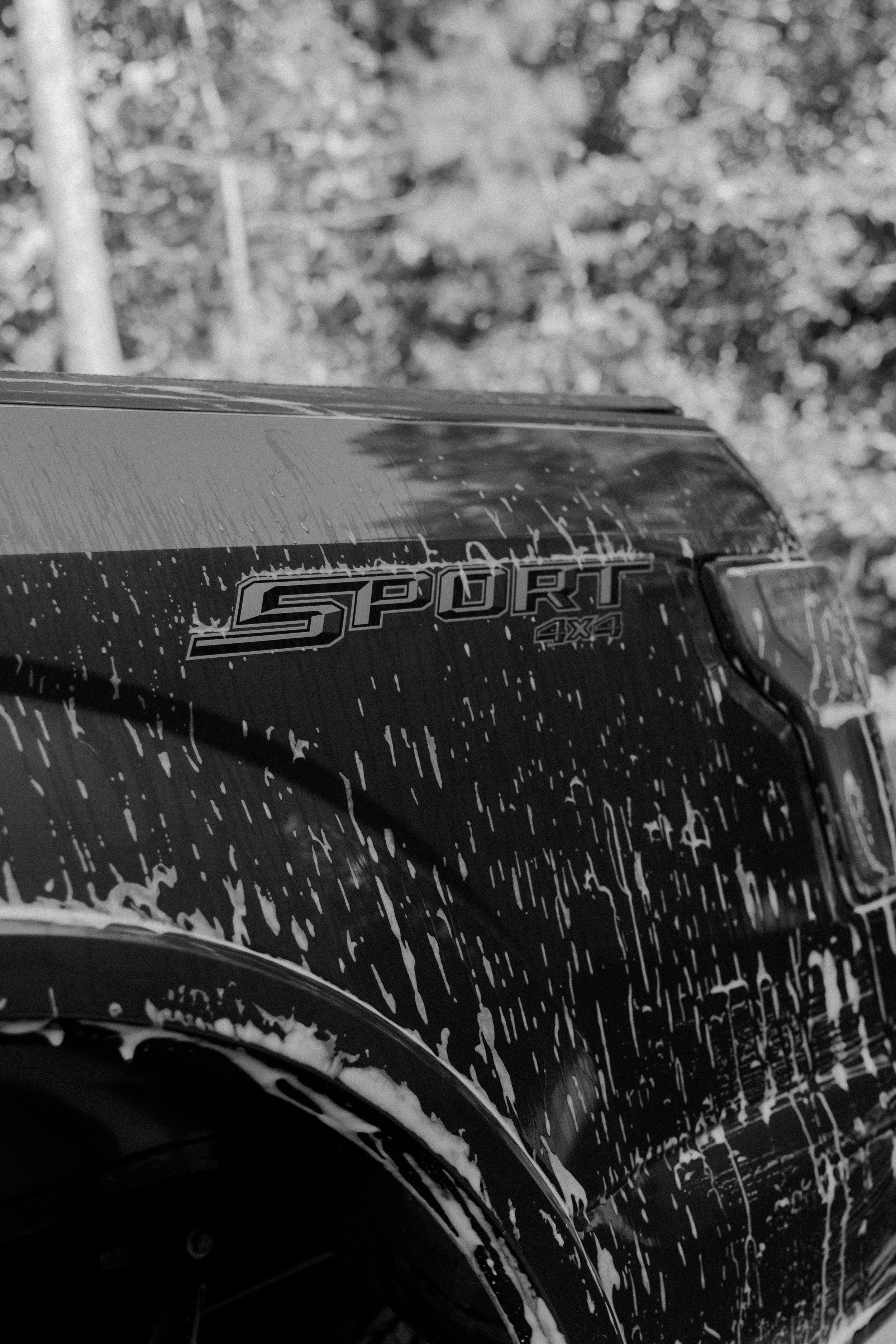 Black and white photo of a soapy SUV Sport badge during a car wash.