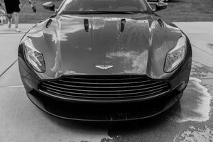 Black and white close-up of a sleek Aston Martin sports car front grille and hood at an outdoor event.