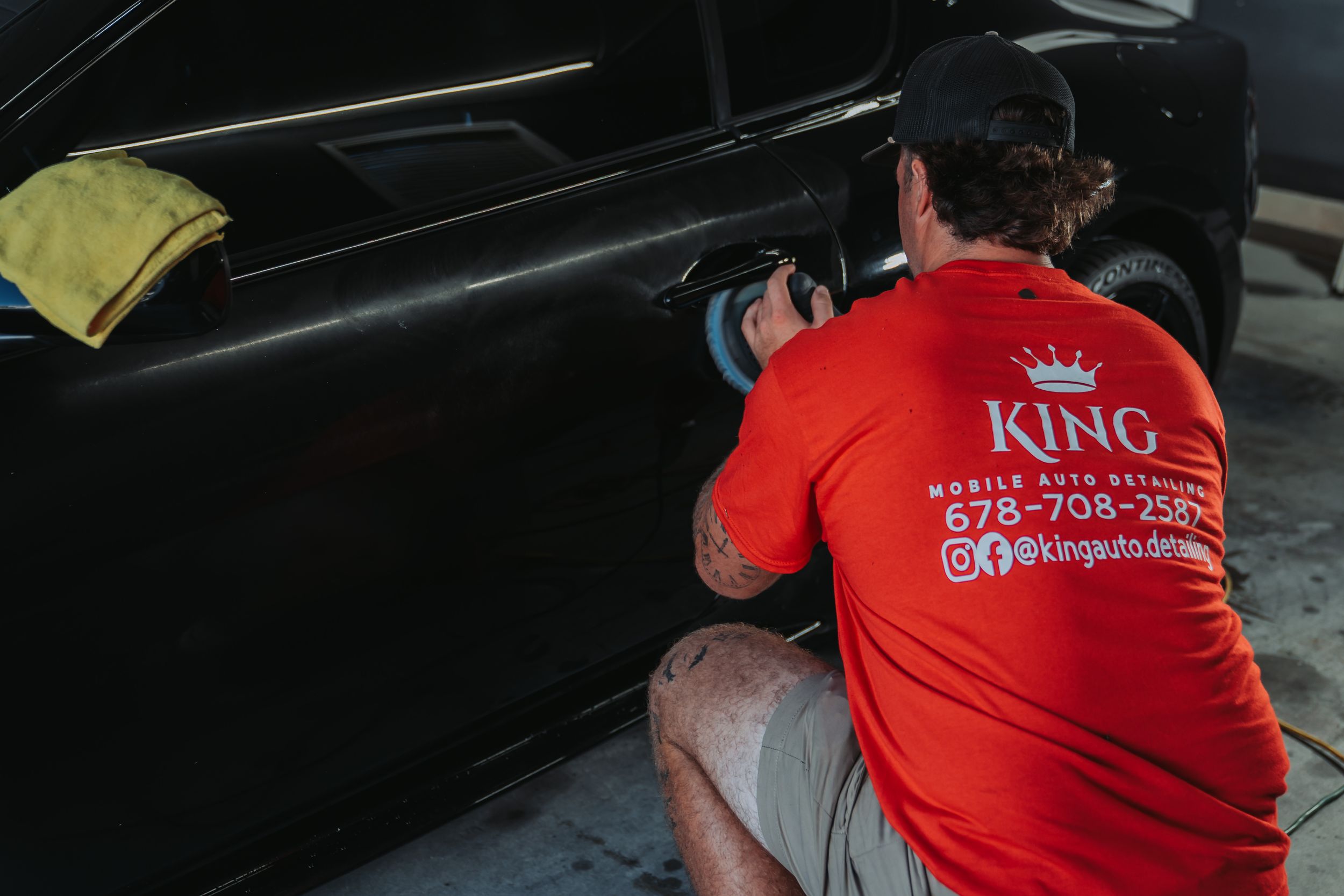 A King Mobile Auto Detailing technician in a red shirt uses a polisher on a black car door.