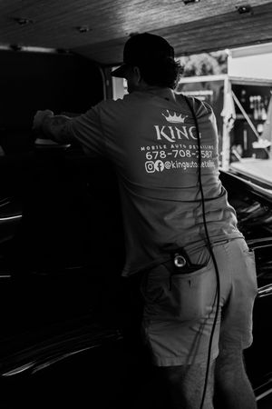 Man in King Mobile Auto Detailing shirt cleaning a black car in black and white photo.