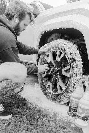 Man scrubbing soapy truck wheel with brush during car wash detailing session outdoors.