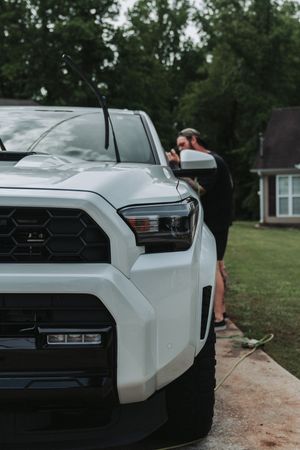 White Toyota Tacoma TRD Pro truck parked in driveway with person washing vehicle near suburban home.