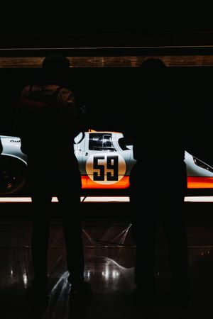 Two silhouettes viewing a Gulf-liveried race car numbered 59 in dark showroom.