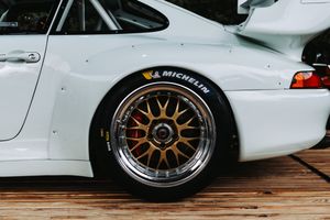 White Porsche race car with gold BBS wheels and Michelin tires on a wooden surface.