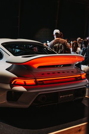 Rear view of white Porsche with glowing orange taillights and spoiler at night event.