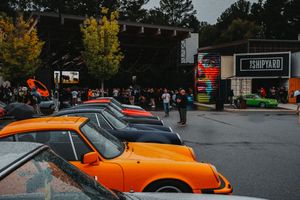 Vintage Porsche cars lined up at an outdoor car show near The Shipyard venue, with crowds gathering among colorful displays.