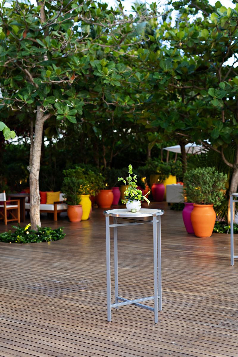 Outdoor deck with tall metal plant stand, colorful orange and yellow pots, lush green trees, and cozy seating area.