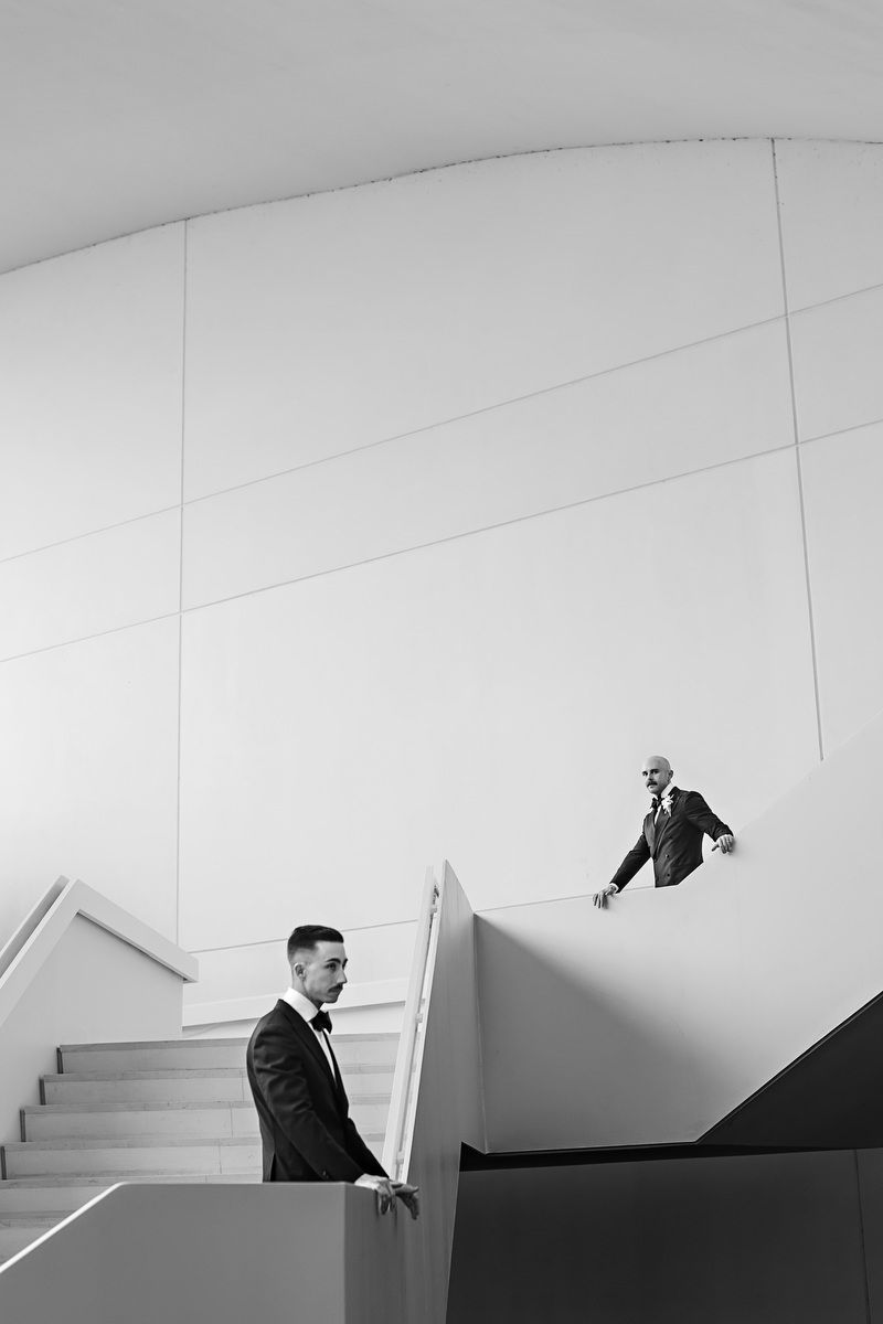 Two men in suits on modern white geometric stairs in a black and white architectural photo.