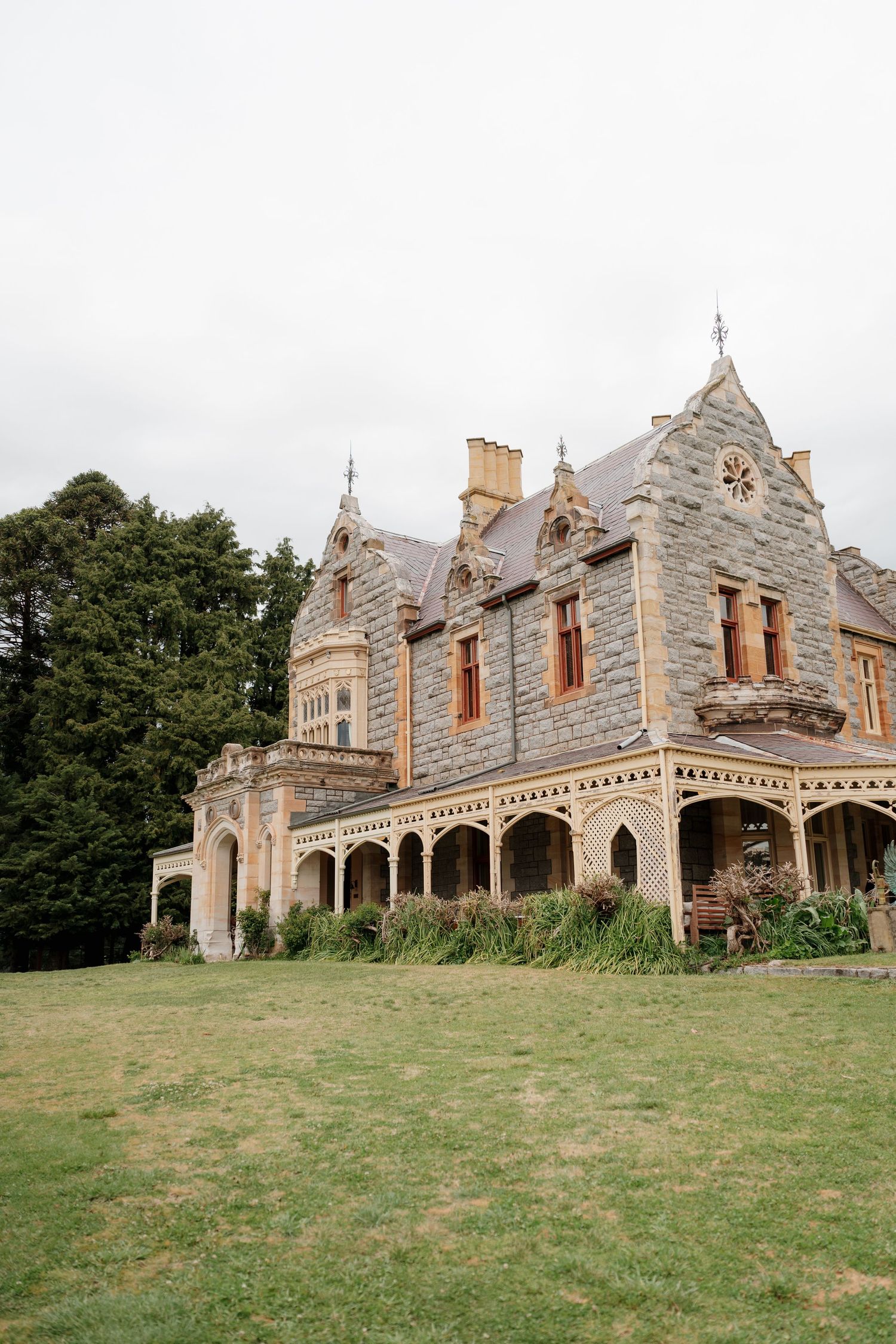 Historic Gothic Revival stone mansion with ornate veranda, pointed gables, and arched windows set against lush green lawns.