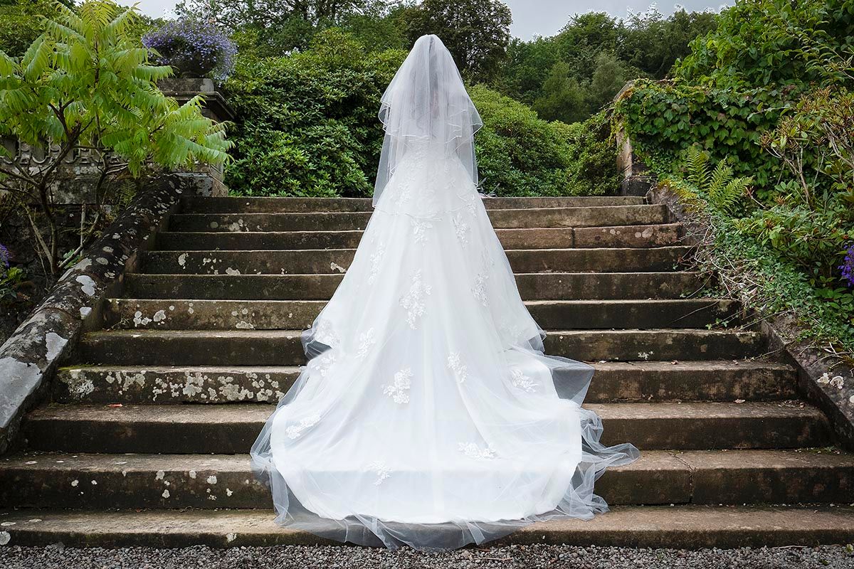 Bride in white wedding gown and veil standing on stone steps at Auchen Castle wedding venue