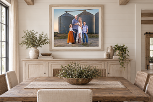 Framed family portrait photo displayed above a farmhouse dining table in a bright, rustic dining room with shiplap walls.