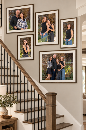 Framed family portrait photos displayed on a staircase wall, featuring professional family and individual photos in dark wood frames.