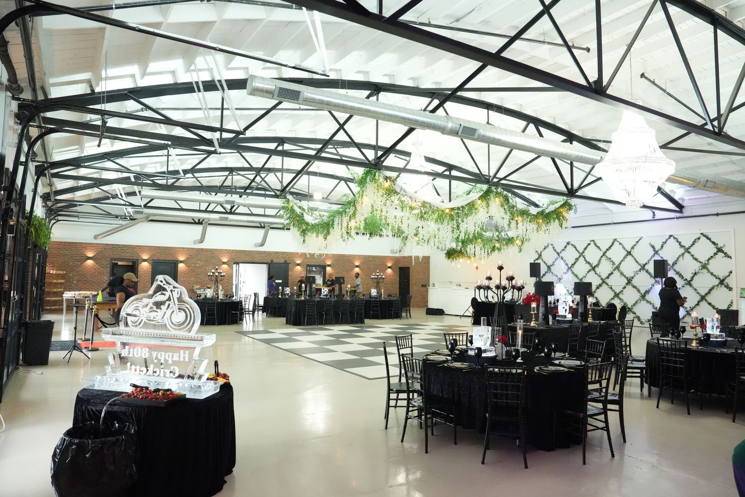 Elegant event backdrop with green and black balloon garland, gold accents, and a framed tuxedo sign on a draped stage.