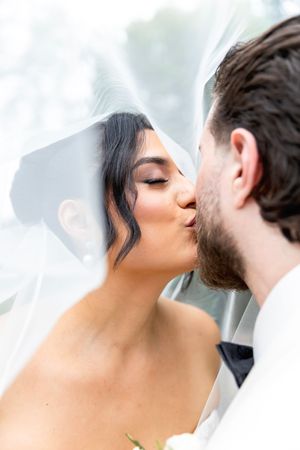 Bride and groom sharing a romantic kiss under a flowing white veil on their wedding day.