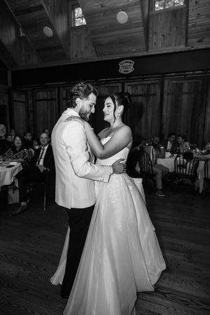 Black and white photo of a bride and groom sharing their first dance at a rustic wedding reception.
