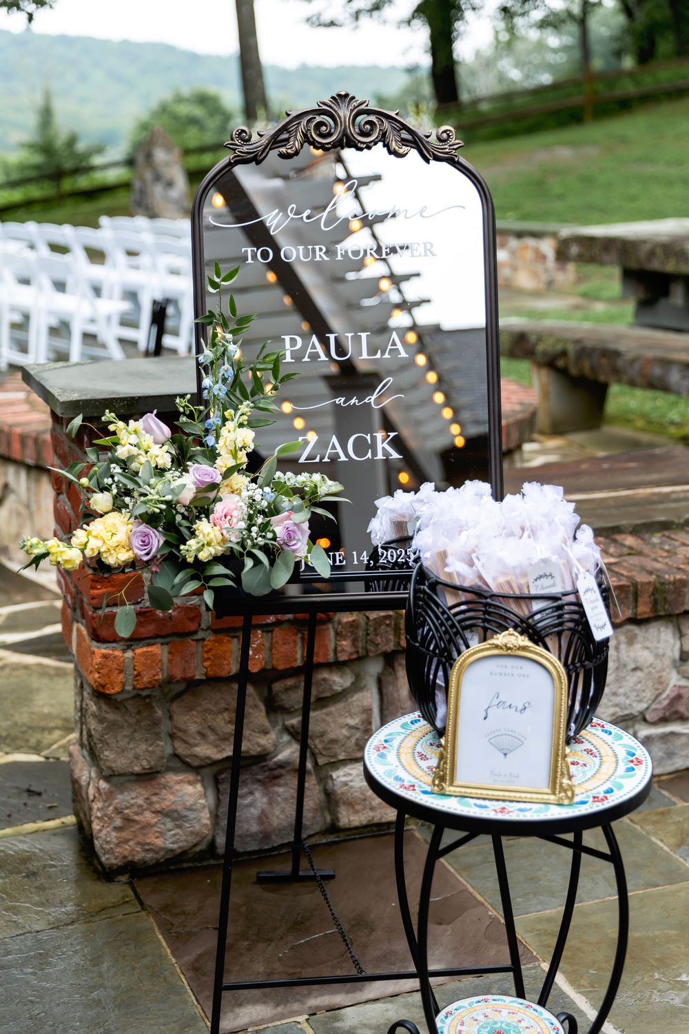 Elegant outdoor wedding welcome mirror sign for Paula and Zack, June 14, 2023, with floral arrangements on stone steps.
