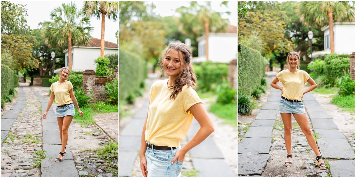 Young woman in yellow top and denim shorts poses on a cobblestone path surrounded by lush greenery.