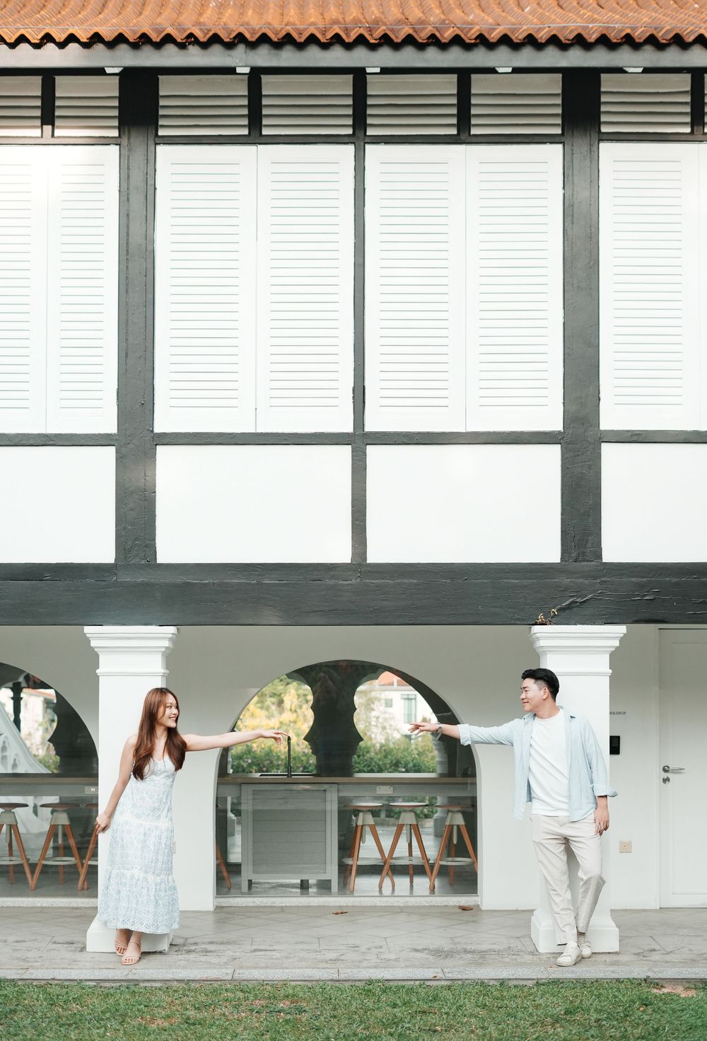 Couple holding hands in front of a white colonial building with arched columns and shuttered windows.
