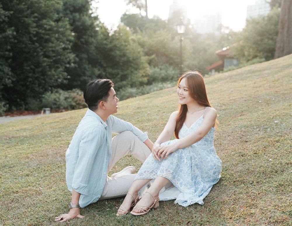 Couple sitting on green grass in a park, sharing a romantic moment in soft golden sunlight.