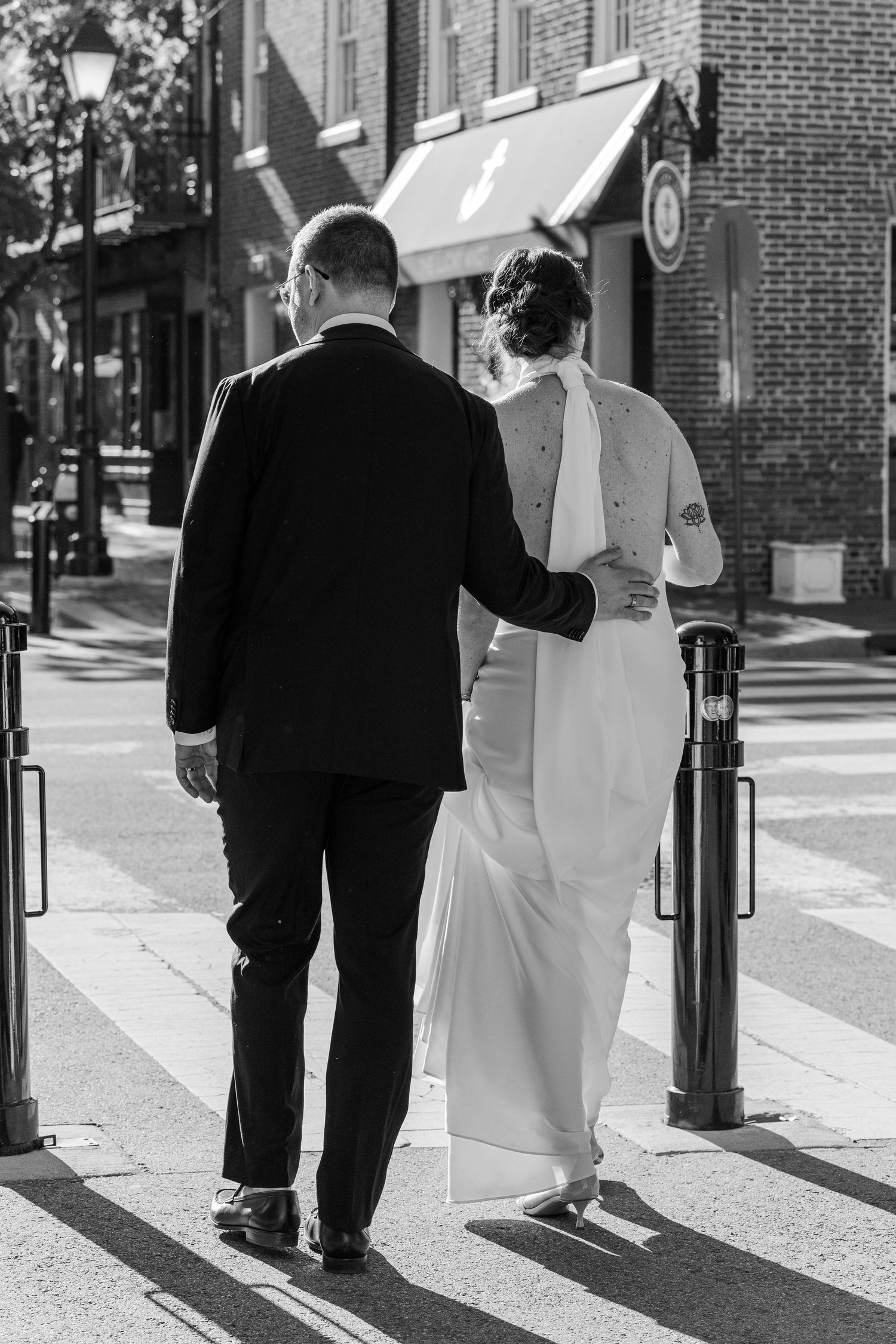 Black and white photo of a bride and groom walking arm in arm across a crosswalk in a charming town street.