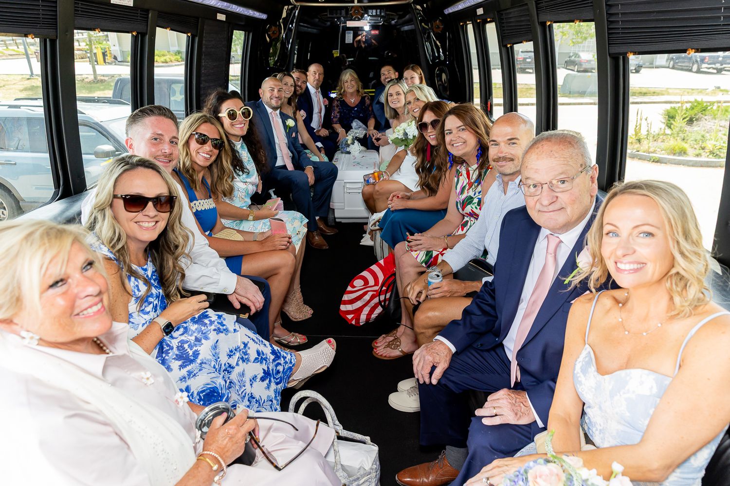 Wedding party guests smiling and posing together inside a decorated party bus on a sunny day.